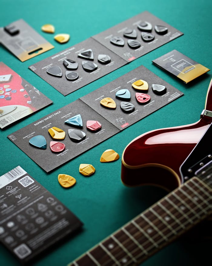 Variety of guitar picks and electric guitar on a green surface; creative musical setup.
