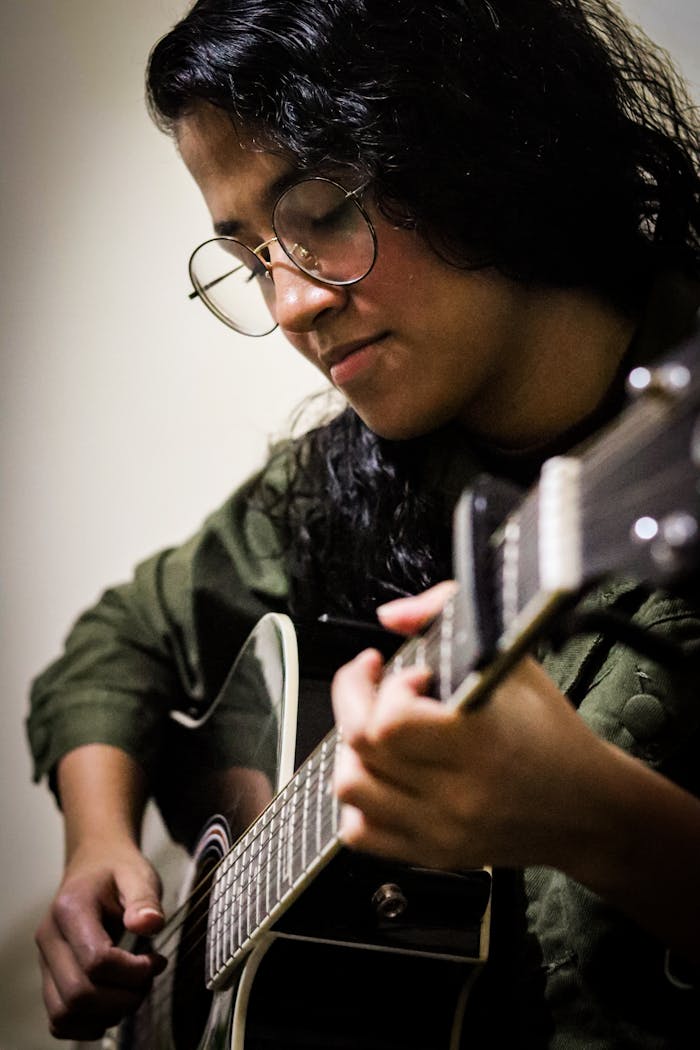 menu-05 A woman focuses while playing an acoustic guitar indoors, expressing passion.