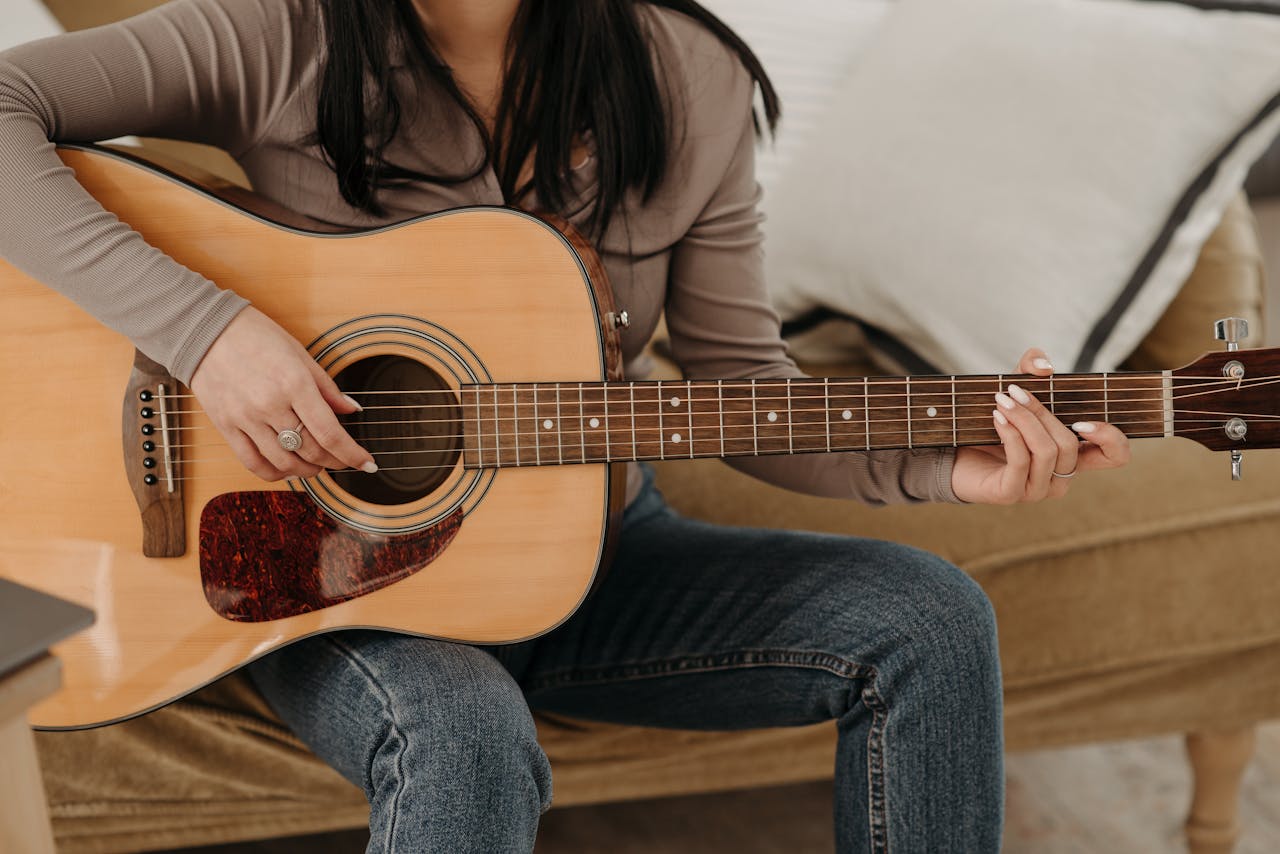 A woman strumming an acoustic guitar while seated in a relaxed indoor setting. Casual and artistic vibe.