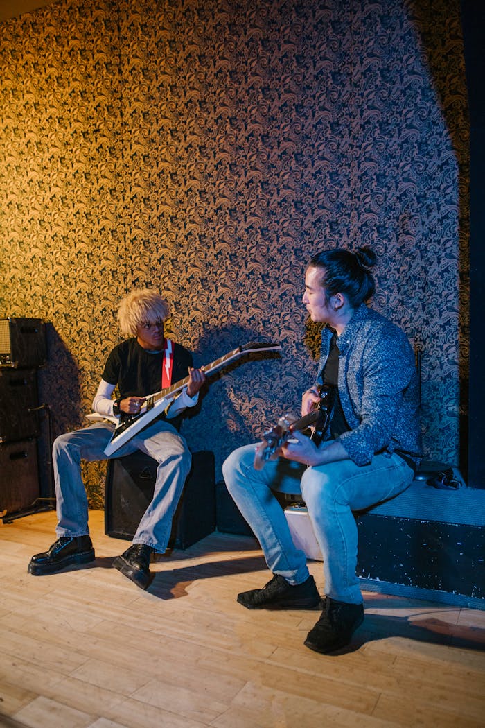 menu-03 Two musicians with electric guitars jamming indoors, seated on stage.