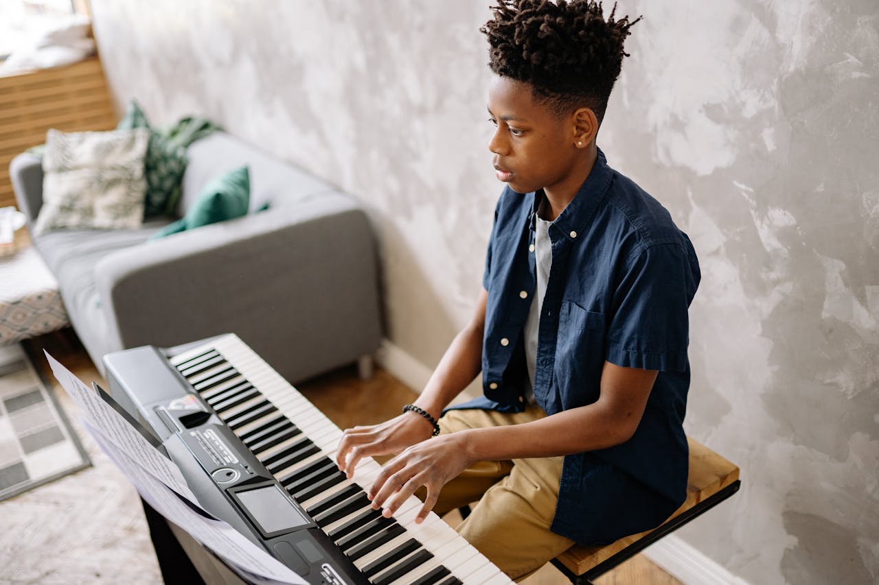 Teenaged boy playing an electronic keyboard indoors, showcasing musical talent and concentration.